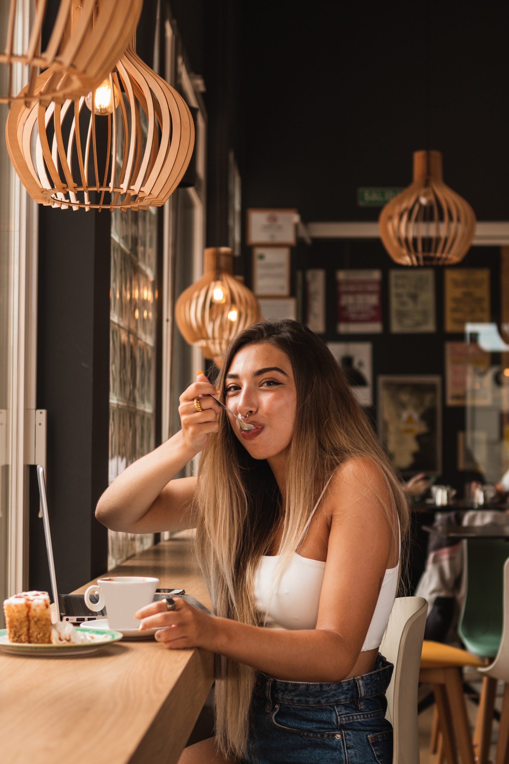 young beautiful blonde and tanned stylish woman eating a pie and working on the computer in a coffee shop