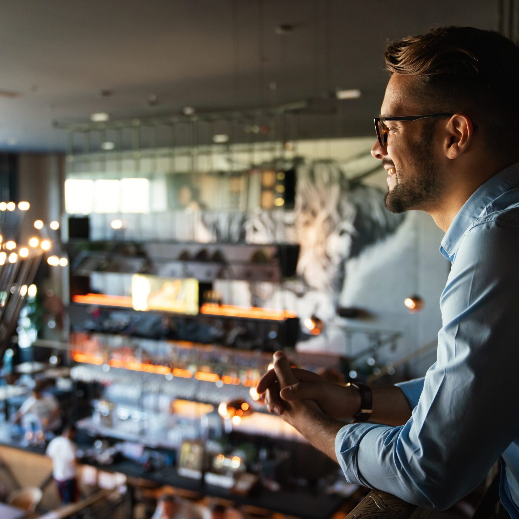 Happy young businessman, restaurant owner proudly looking at crowded restaurant
